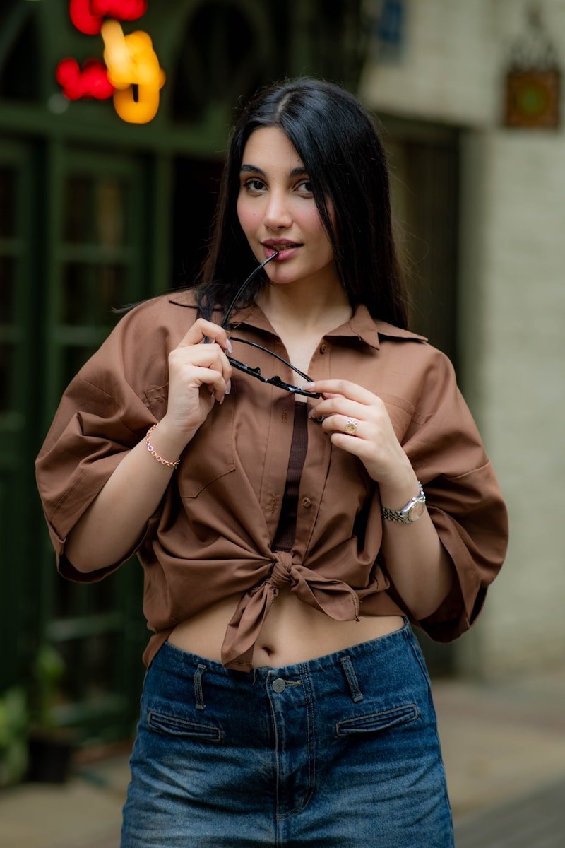 Woman in brown shirt and denim shorts holding sunglasses